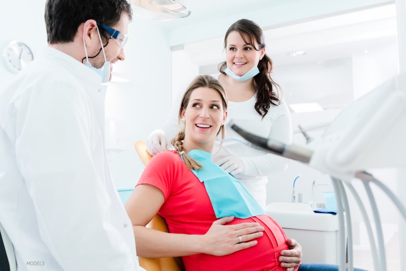 Femme enceinte assise dans un cabinet de dentiste avec dentiste et infirmière